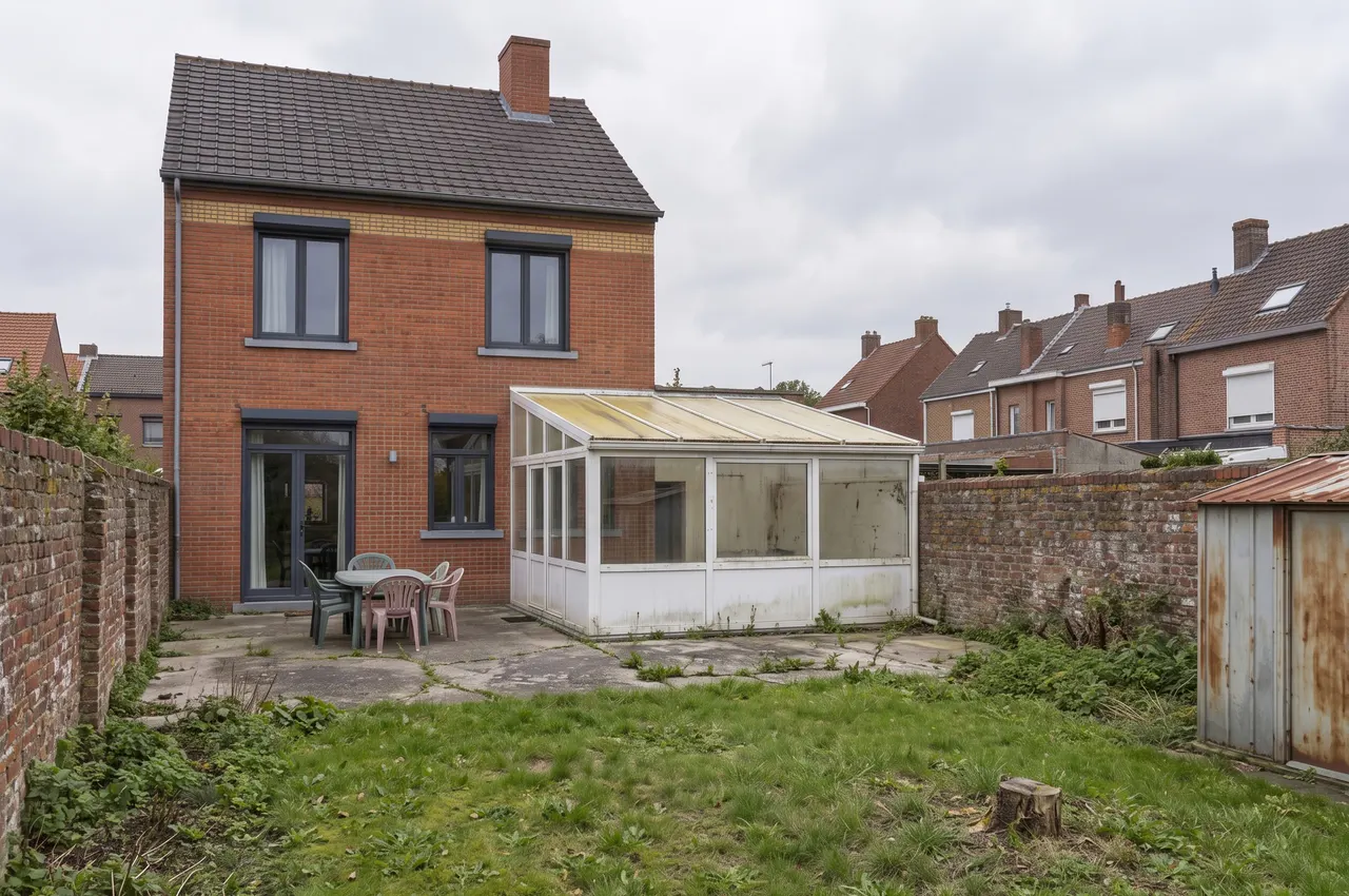 Le même jardin avant les travaux : véranda en PVC au toit jauni, terrasse en béton fissurée et abri de jardin rouillé