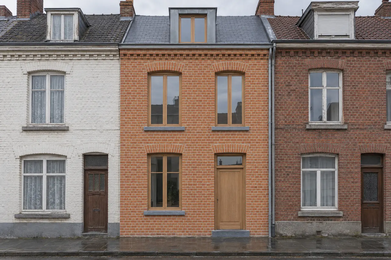 Façade sur rue de la maison après travaux : brique nettoyée, fenêtres et porte en chêne, appuis en pierre bleue, entre deux maisons voisines plus anciennes