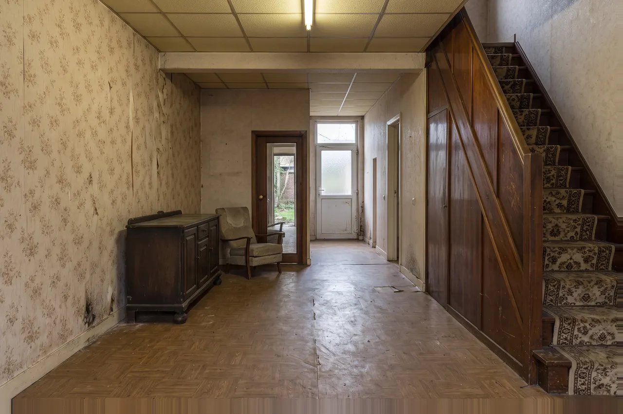 Le même rez-de-chaussée avant les travaux : mur porteur percé d’une porte étroite, papier peint à fleurs, faux plafond et escalier coffré de bois verni